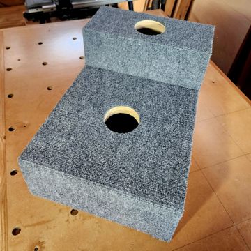 Two grey carpeted speaker boxes with circular cutouts on a wooden table.