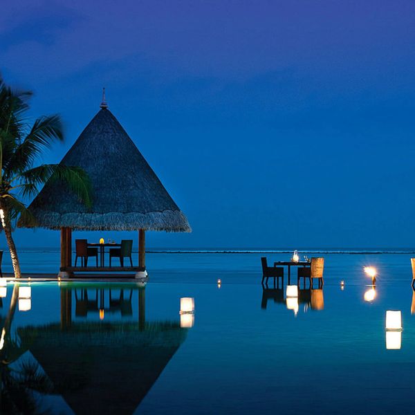 Romantic lakeside dining with lanterns and a thatched gazebo at dusk.