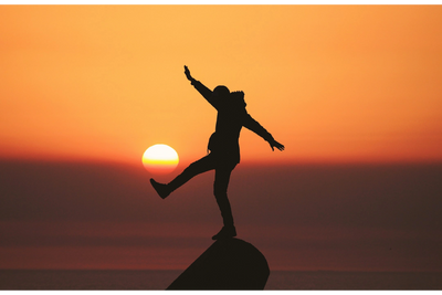 Silhouette of person balancing on rock against orange sunset.