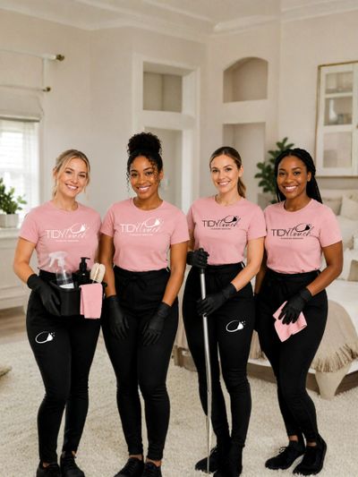 Four cleaning professionals in matching uniforms smiling indoors.