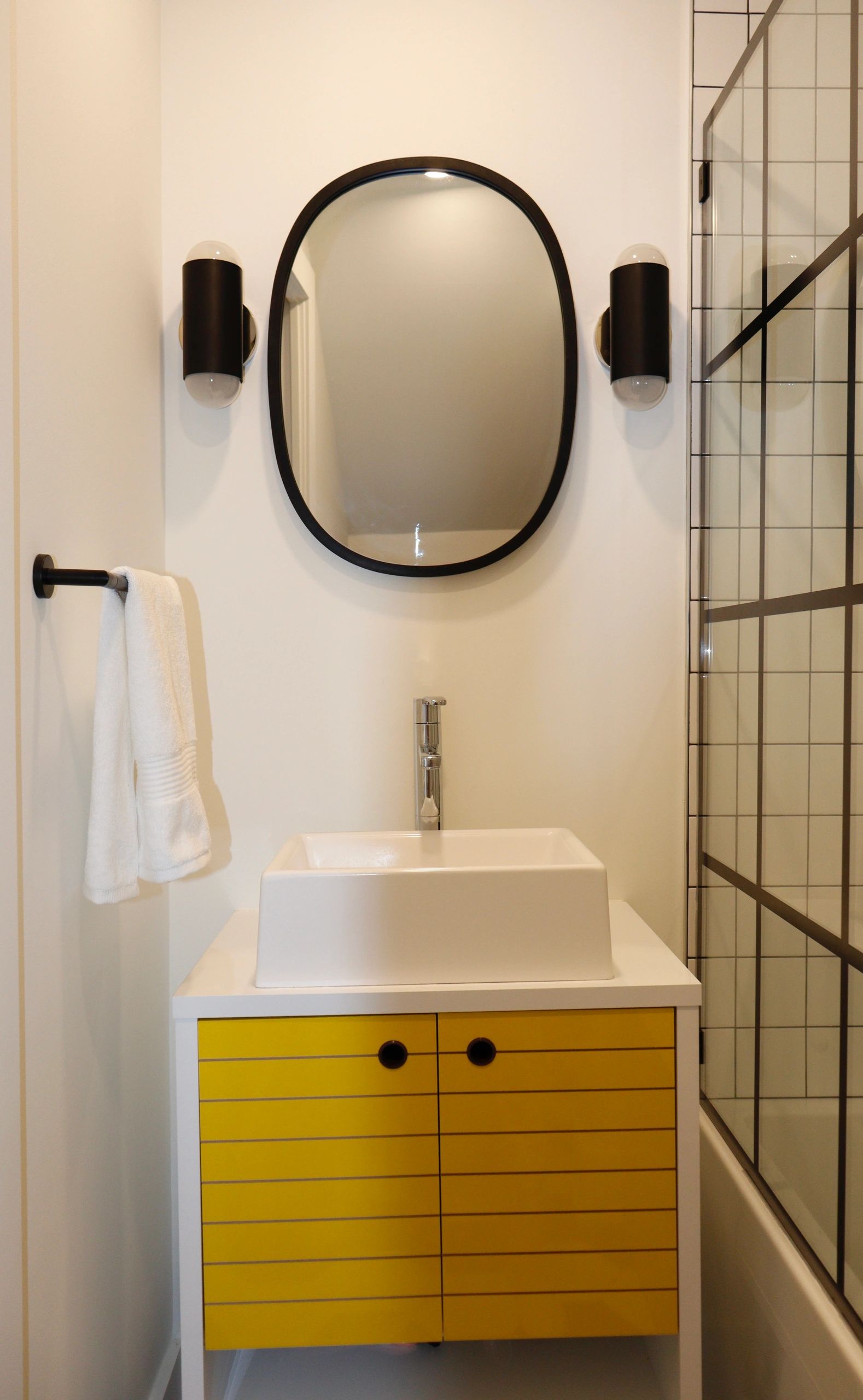 Modern bathroom with yellow vanity and oval mirror.