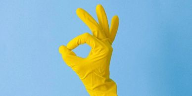 Hand in a yellow glove making an OK sign against a blue background.