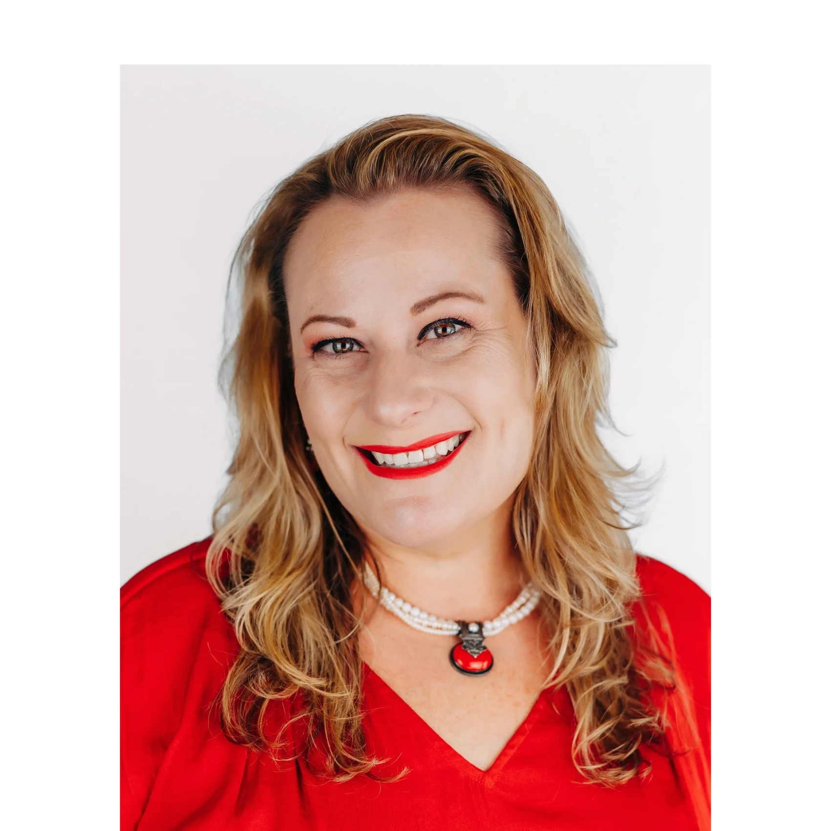 Smiling woman in red top with pearl necklace and red pendant.