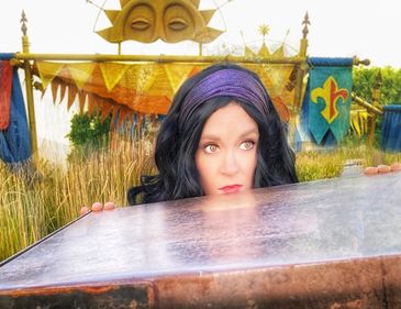 Women dressed as Esmerelda hiding behind a wall with festival decor behind her