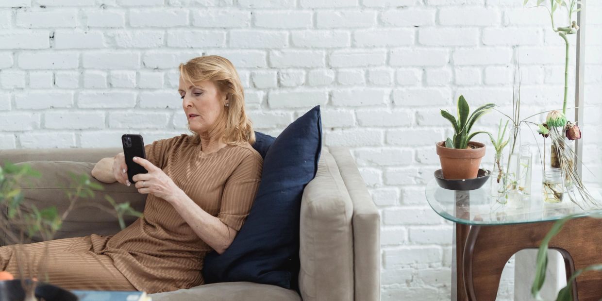 Woman lounging on couch, focused on her smartphone in a bright, plant-filled room.