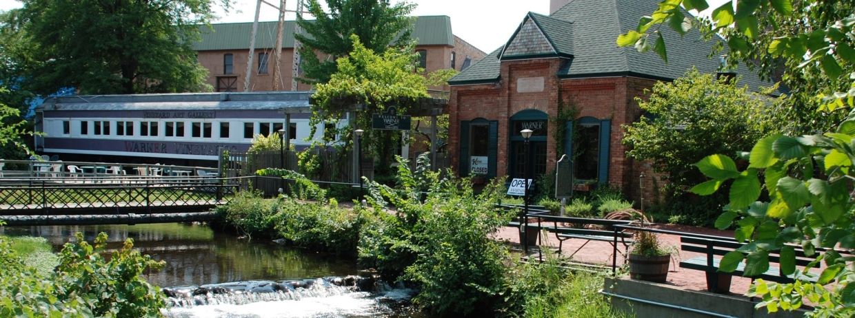 Stream and greenery beside brick buildings and a railway car.