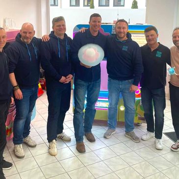 Group of men posing indoors with gaming machine in background.