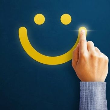 Hand drawing a glowing smiley face on a dark background.