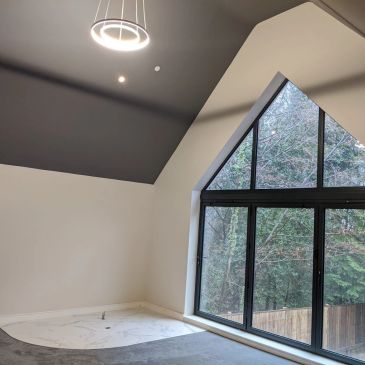 Empty modern room with large triangular window and circular ceiling light.