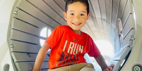 Smiling boy in an orange shirt inside a playground tunnel.