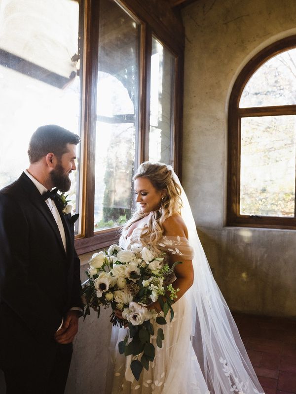 Bride and groom hold hands while holding a large bridal bouquet in fresh flowers. 