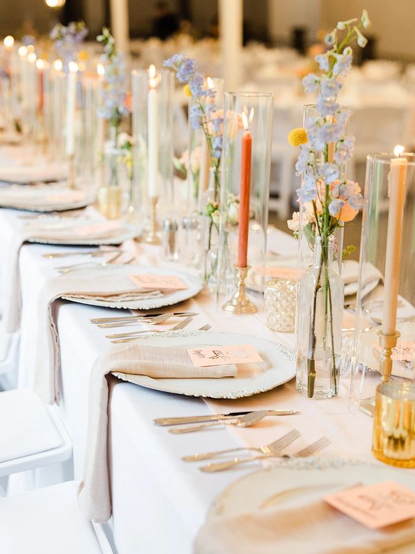 Estate table with bud vases, flowers, candles, table settings and decor for wedding reception. 