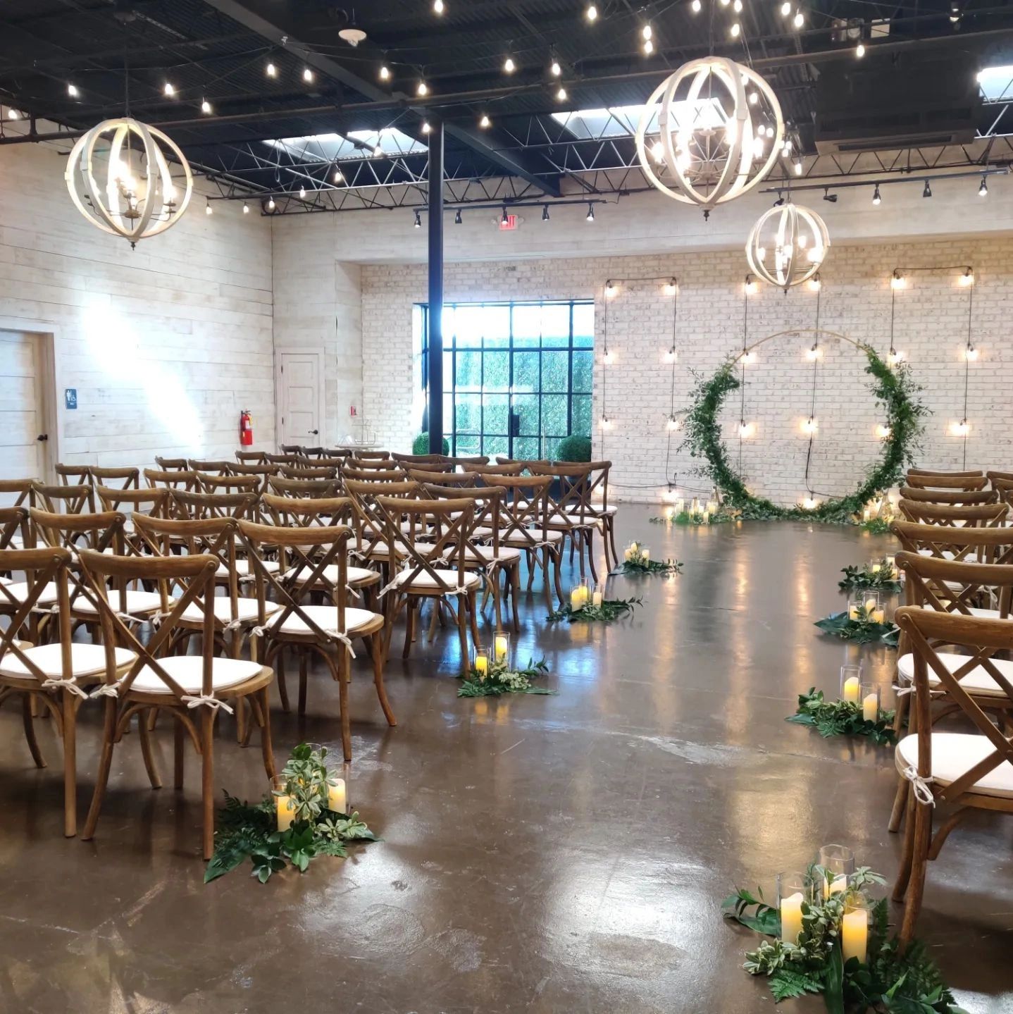 Wedding ceremony crossback chairs with cushions, arbor with greenery, string lights, aisle markers. 