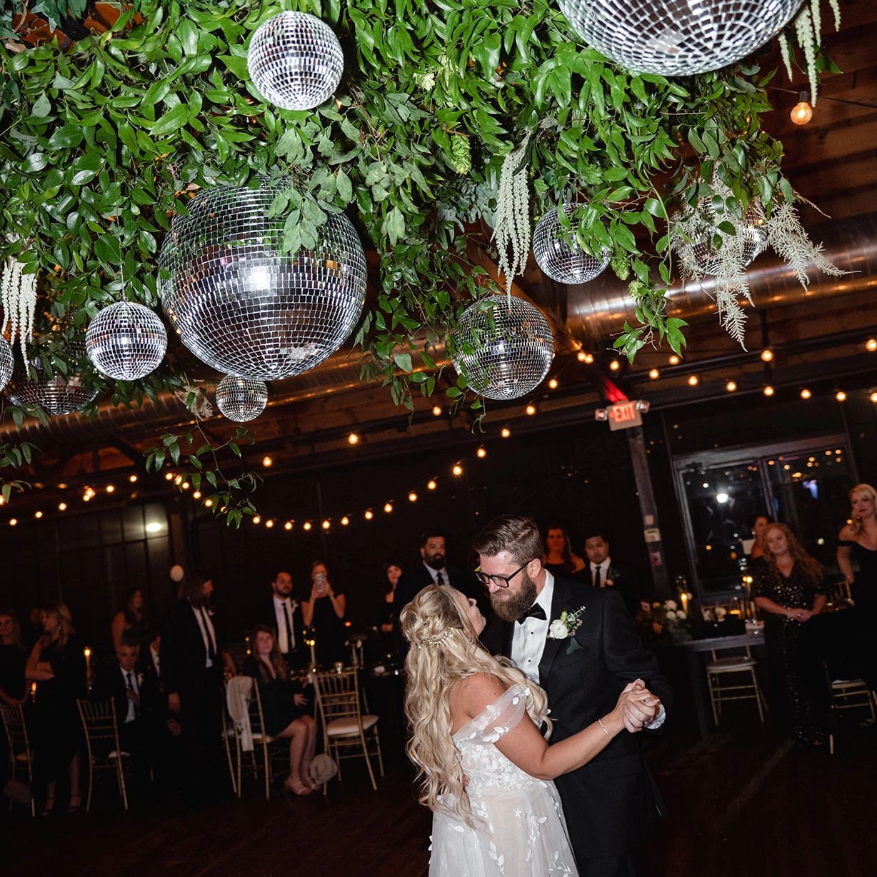 Bride and groom dance under a disco ball and fresh greenery installation in Georgia venue. 