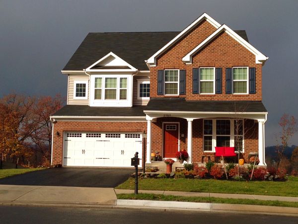 Two-story brick house with white garage doors and red front door.
