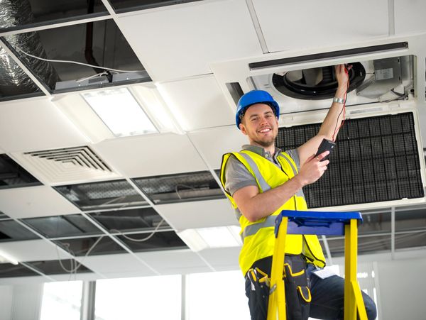 Electrician fitting air conditioning to office interior