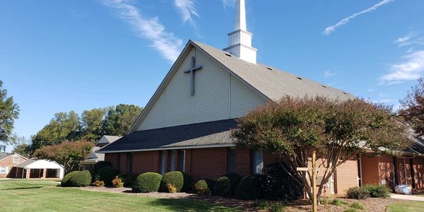 A brick church with a white steeple and cross under a blue sky.