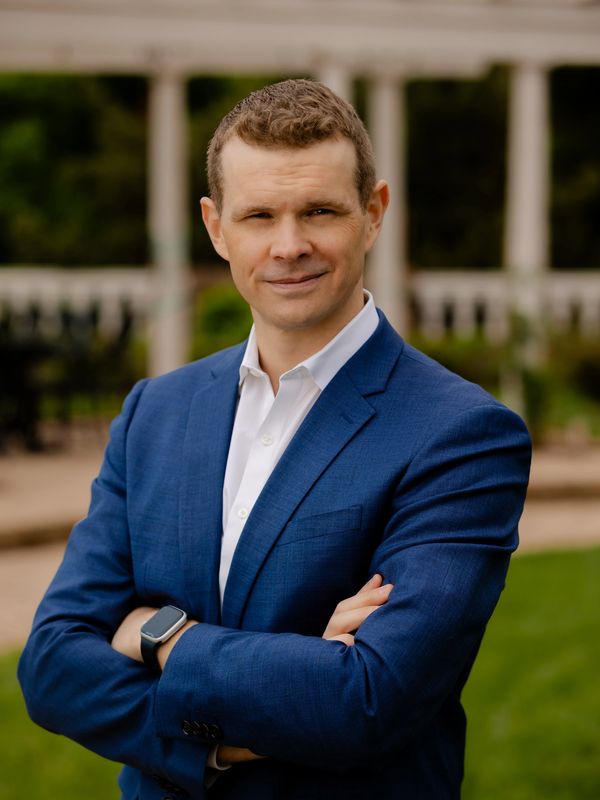 Confident man in a blue suit outdoors with arms crossed.