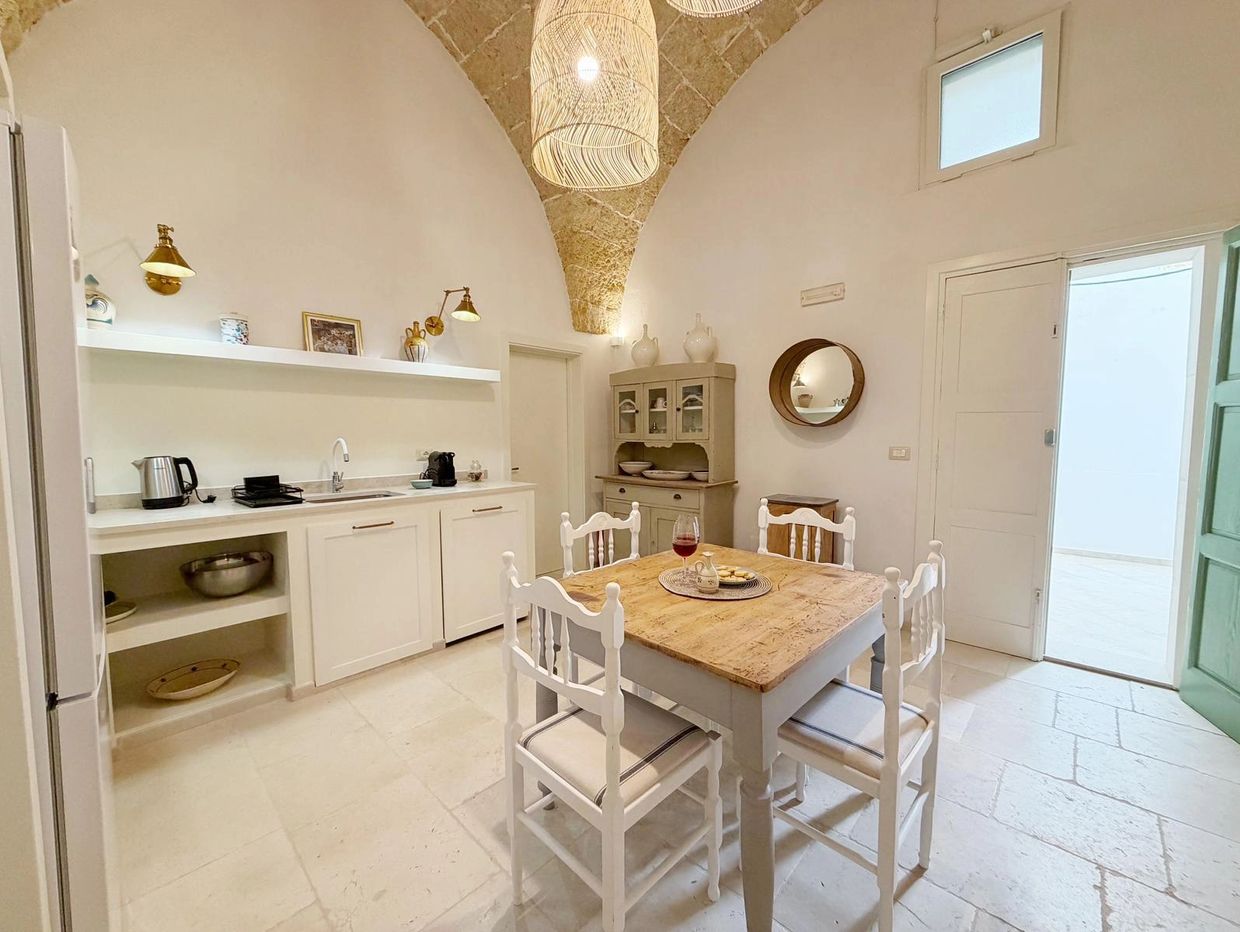 Bright rustic kitchen with a wooden dining table and white chairs under a stone vaulted ceiling.