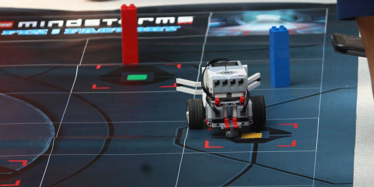 A LEGO Mindstorms robot on a blue game mat with red and blue block towers.