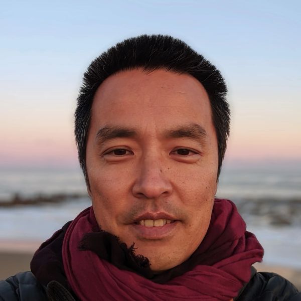 A man wearing a maroon scarf with a beach sunset background.