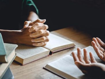 Two people engaged in discussion over open books with clasped hands.