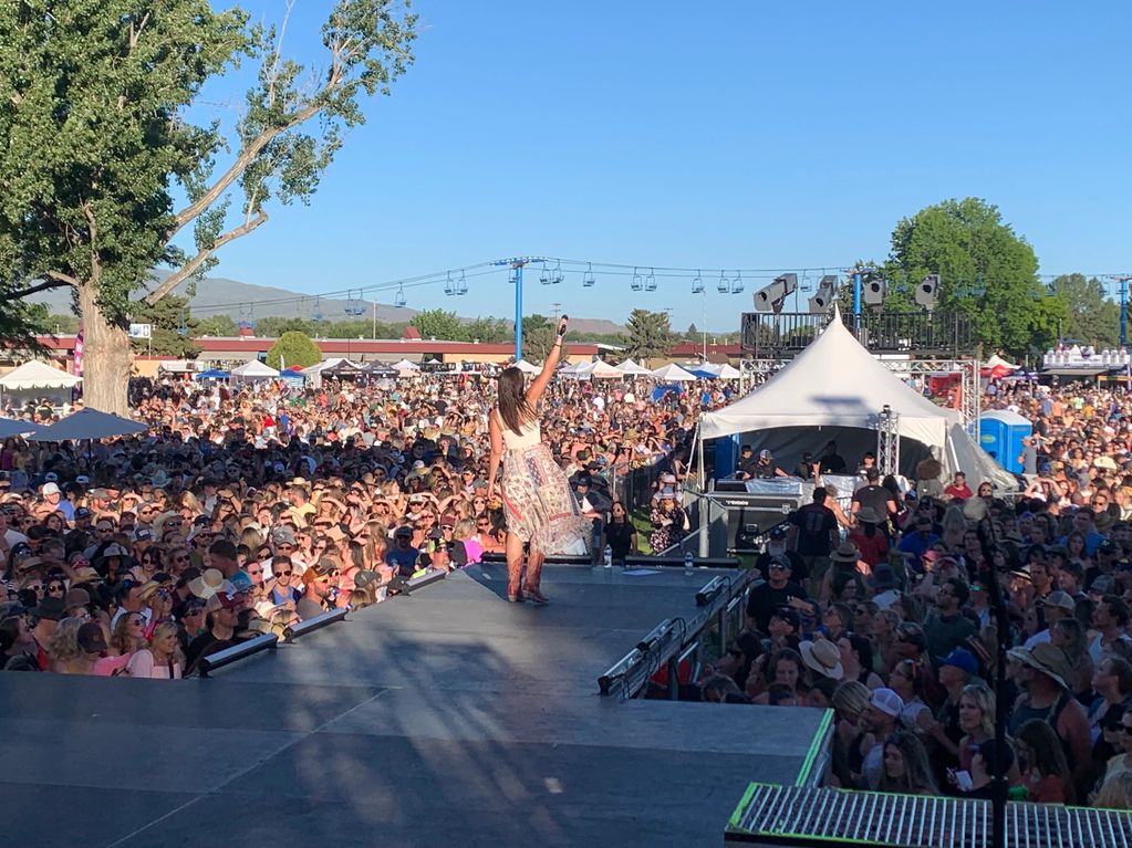 Female singer performs for a large outdoor festival crowd under a clear sky.