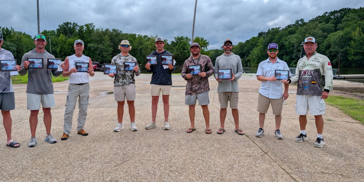 Group of men outdoors holding certificates, standing in a line on a cloudy day.