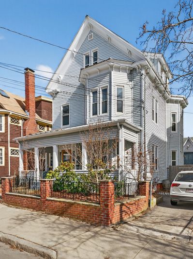 Three-story white house with a brick fence and front porch.