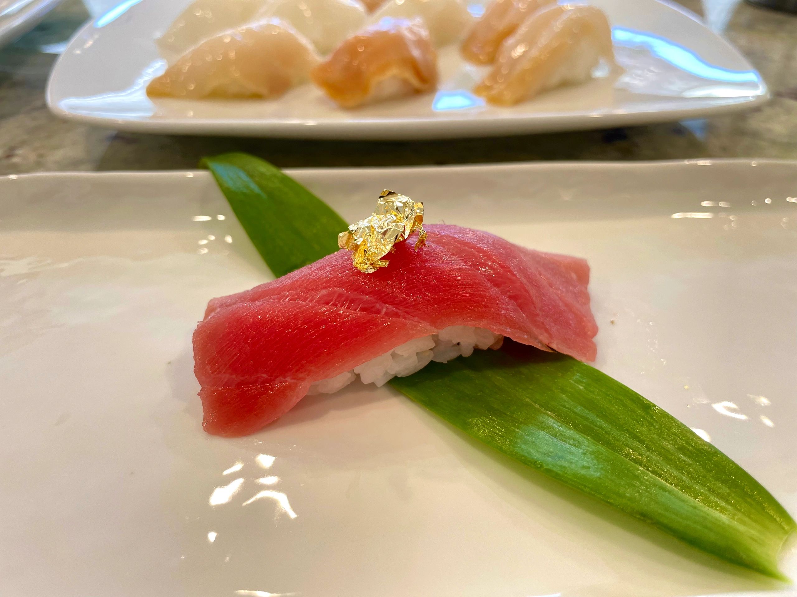 Sushi piece with a slice of pink fish and gold leaf on a green leaf.