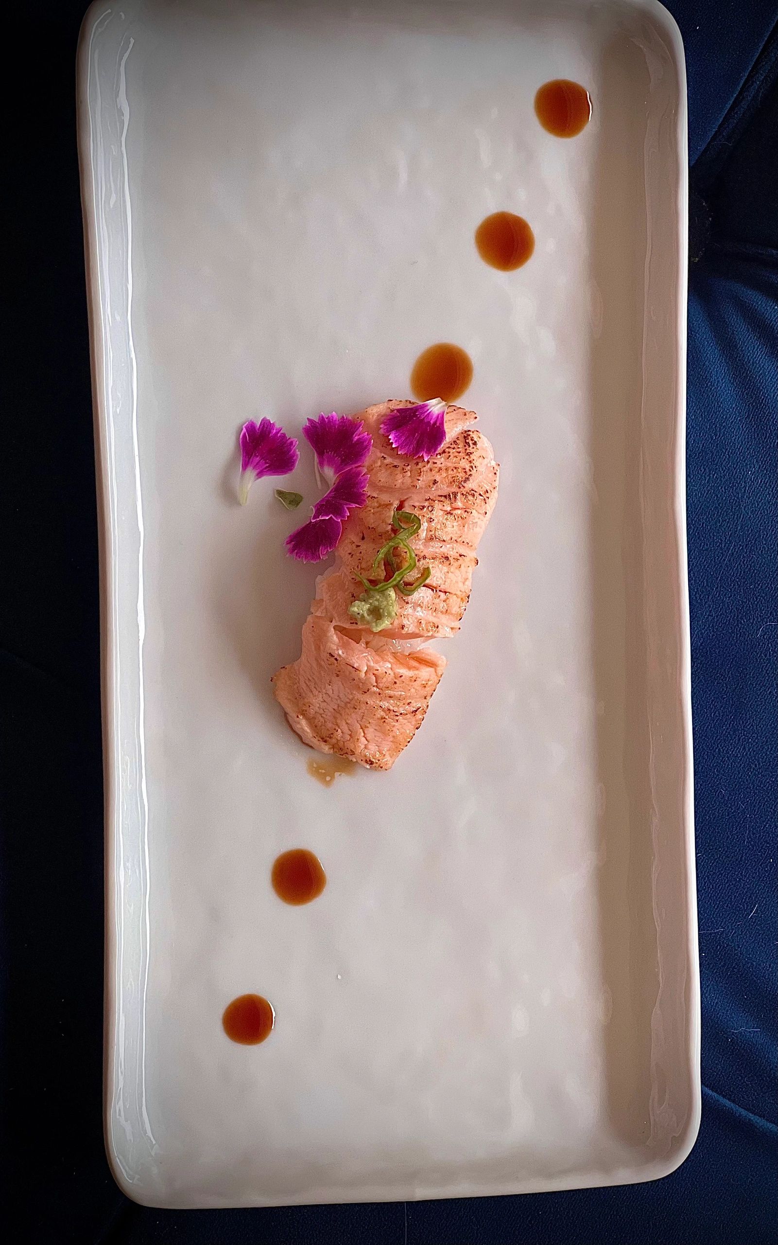 Grilled salmon with edible flowers and sauce drops on a minimalist white plate.