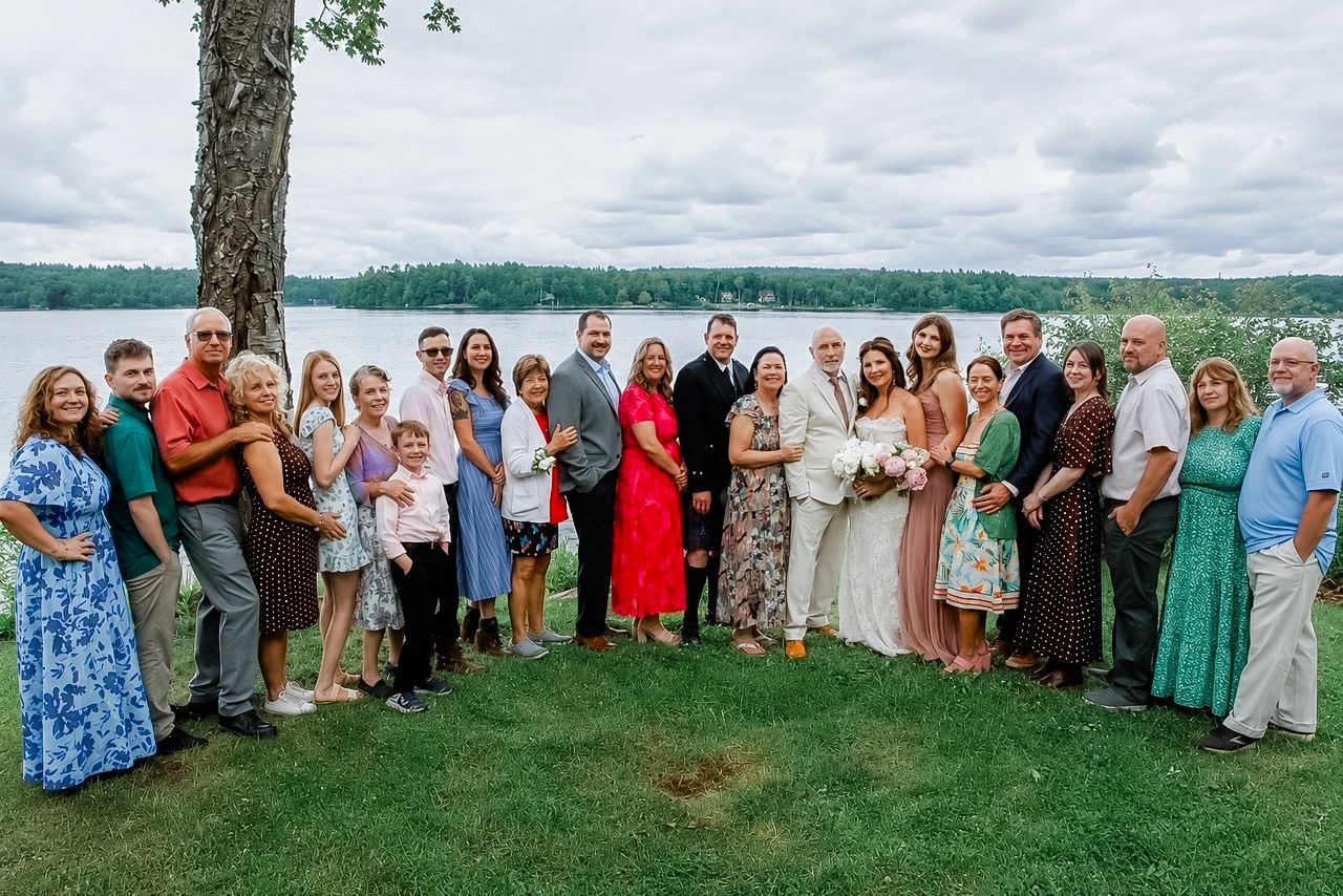 Large group photo by a lake at a wedding.