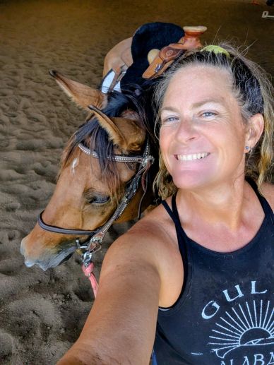 Woman smiling with a saddled horse indoors.