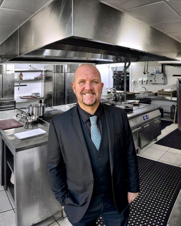 A smiling man in a suit stands in a professional kitchen.