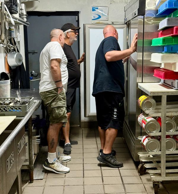 Three men inspecting a commercial kitchen refrigerator.
