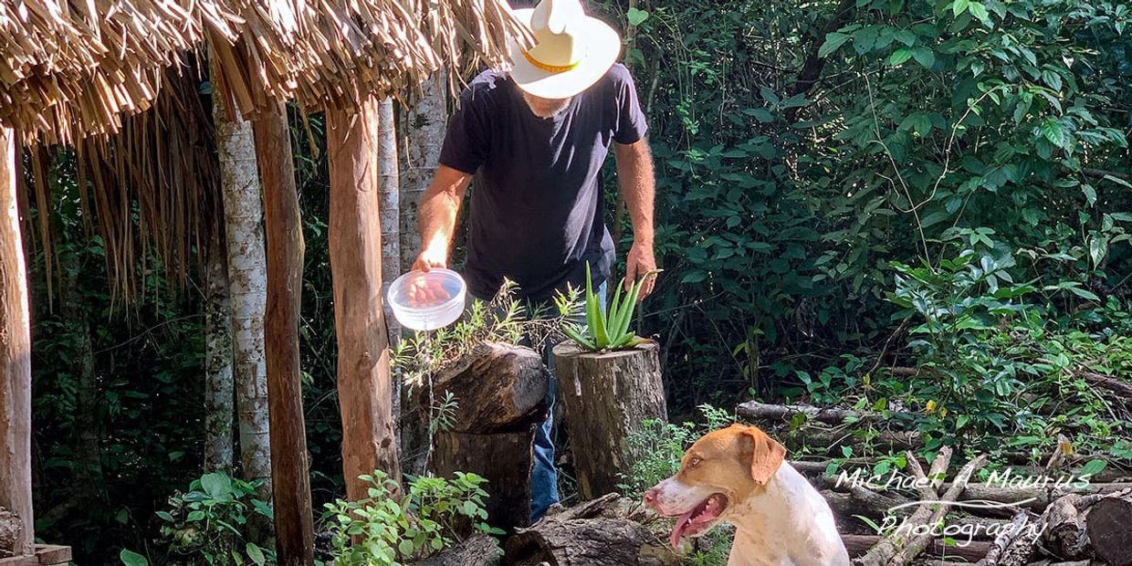 Michael A. Maurus in front of his hut with his dog Bruno, watering the medicinal herbs.