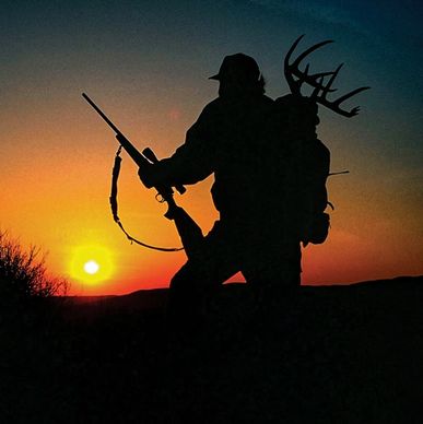 Silhouette of a hunter carrying a rifle and deer antlers at sunset.