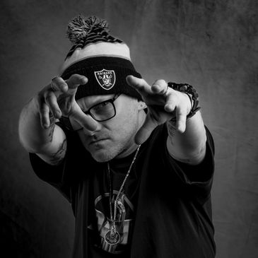 Man wearing Raiders beanie and glasses reaching forward with intense expression.