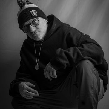 Rennie Foster wearing a Raiders beanie and glasses, squatting in a black hoodie and sneakers.