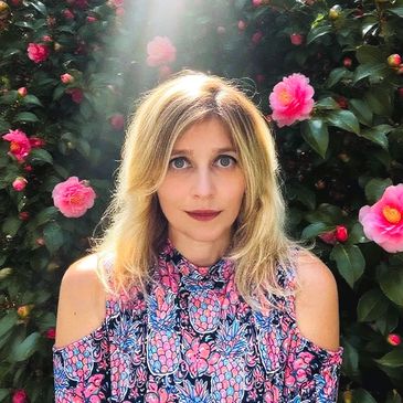 Woman with blonde hair in floral dress surrounded by pink flowers.