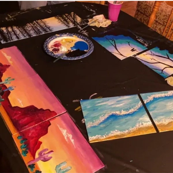 Multiple landscape paintings on a table with art supplies.