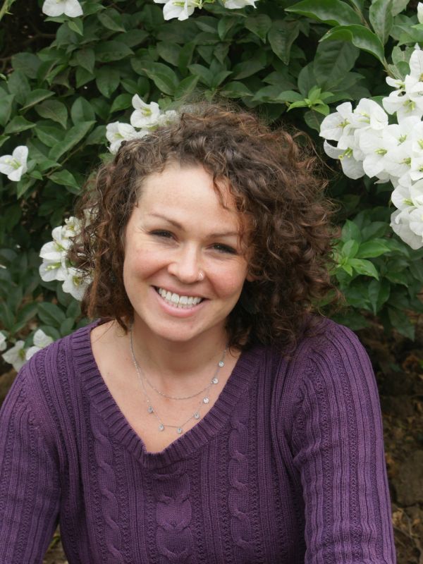 Smiling woman with curly hair in purple sweater outdoors.