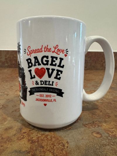 White mug with bagel shop logo and slogan.