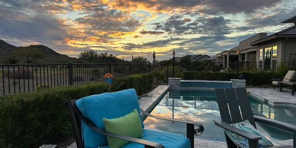 Cozy poolside seating with vibrant cushions under a colorful sunset sky.