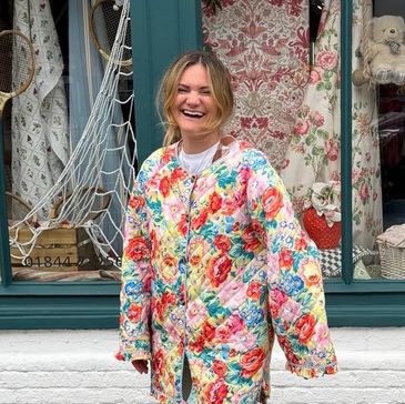 Woman in a colorful floral jacket smiling outside a shop window.