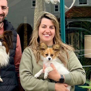 A smiling woman holding a small dog outdoors.