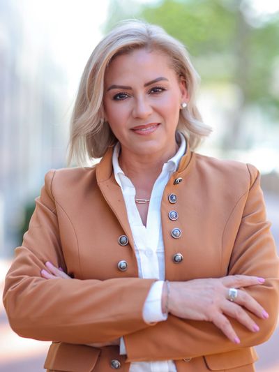Confident woman in a brown jacket smiling with folded arms.