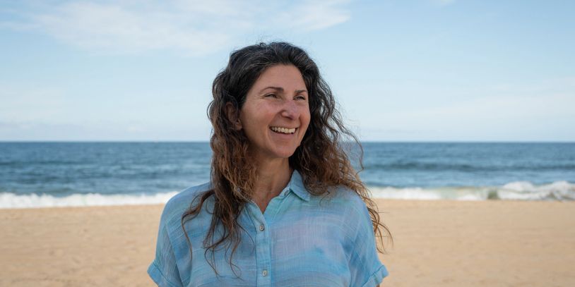 Woman smiling on a beach with ocean in the background.