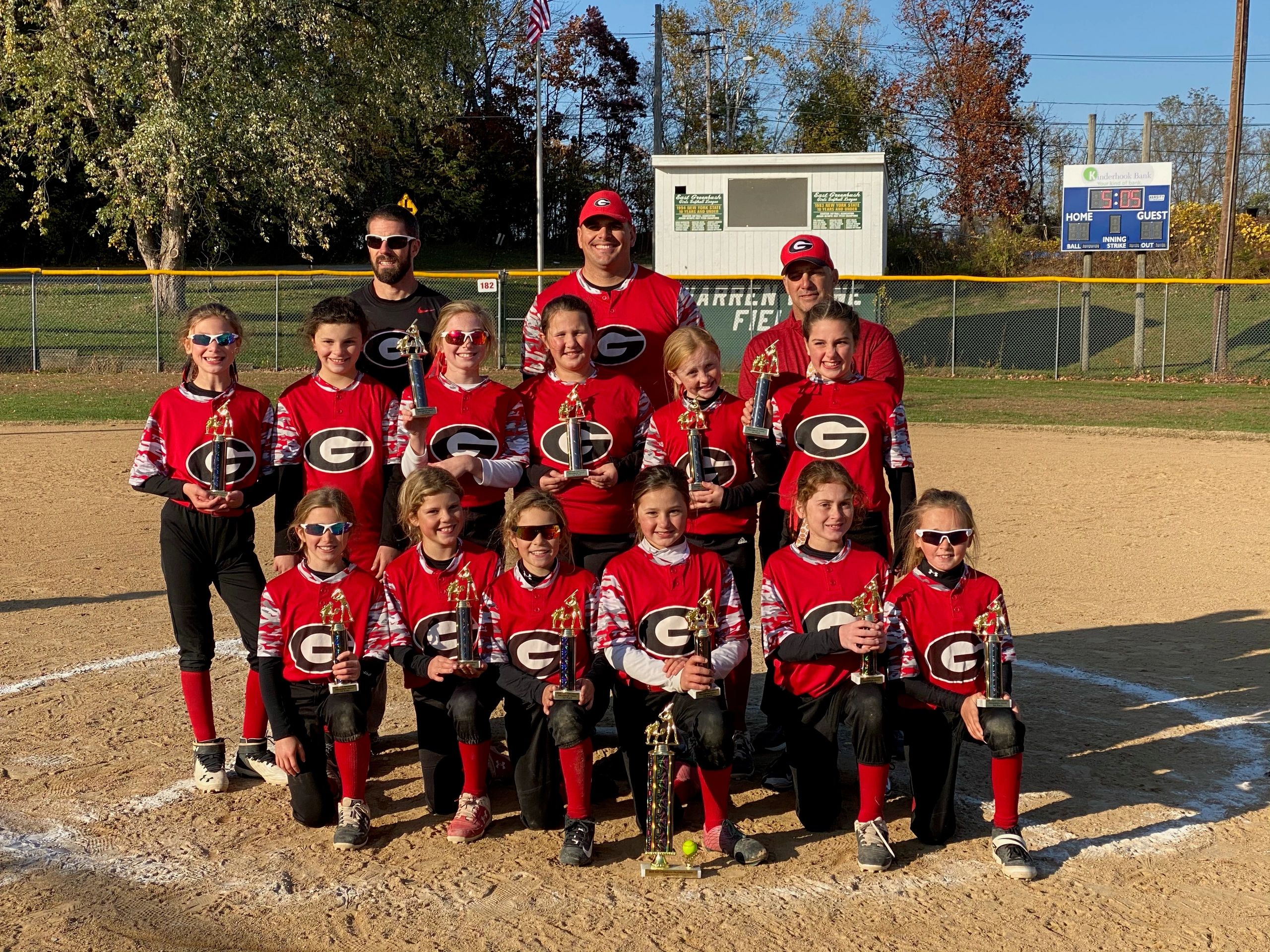 Youth softball team posing with trophies on a sunny field.