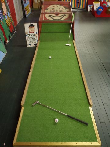 Vintage mini-golf putting green with clown face target and clubs.